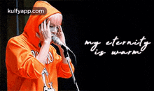 a person in an orange hoodie is singing into a microphone with the words `` my eternity is warm '' written above them .