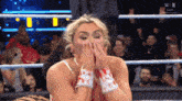 a woman in a wrestling ring covers her mouth with her hands