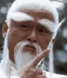a man with a long white beard and mustache is pointing his finger at something .