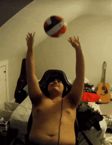 a shirtless man is playing with a volleyball in a bedroom