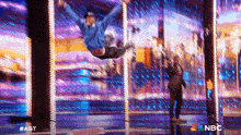 a man in a blue shirt is jumping in the air on a stage in front of a nbc sign