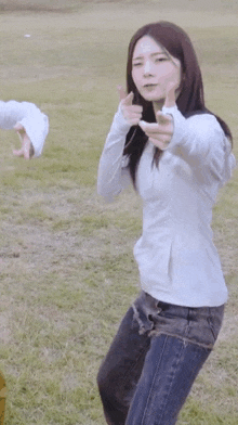 a woman in a white jacket and jeans is standing in a field and giving a thumbs up .