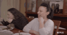 two women are sitting at a table with netflix written on the bottom