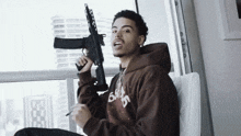 a young man in a brown hoodie is holding a gun