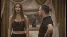 a man and a woman are standing next to each other in a living room in front of a mirror .