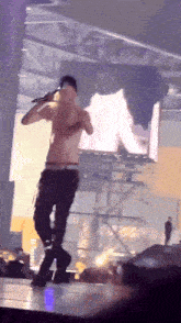 a shirtless man singing into a microphone on stage