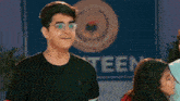 a boy wearing glasses is standing next to a girl in front of a sign that says teen .