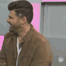 a man with a beard wearing a brown jacket and a white shirt is smiling .