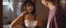 a man and a woman are standing next to each other in a kitchen . the woman is holding a bowl of food .