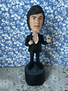 a bobble head of a man in a suit holds a microphone