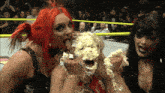 a woman with a cake on her face is surrounded by two women