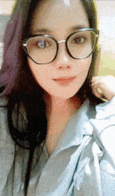 a woman wearing glasses and a blue shirt looks at the camera