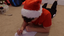 a boy wearing a santa hat is writing on a piece of paper