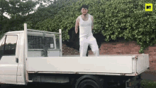 a man in a white tank top is standing on the back of a truck