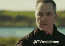 a man in a black jacket stands in front of a body of water with the words @tvresidence below him