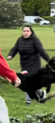 a woman in a black coat is holding a black dog in her arms