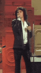 a man singing into a microphone while wearing a white shirt and a black jacket
