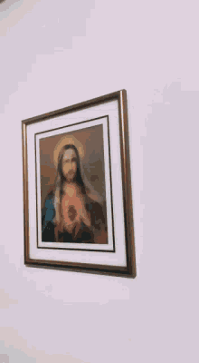 a framed picture of jesus holding a heart on a pink wall
