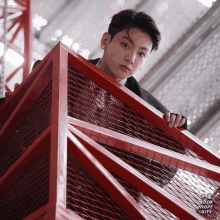 a man in a suit stands behind a red metal fence with the words kook jhope on the bottom