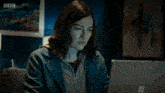 a woman is sitting at a desk with a bbc logo on the bottom left
