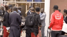 a group of people are standing outside of a building and one of them is wearing a red jacket with a lion on it