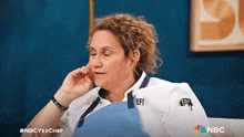 a woman in a chef 's uniform is sitting on a couch with a nbc logo in the background