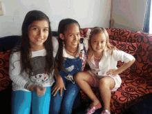 three girls are posing for a picture on a red couch