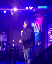 a man stands on a stage with a microphone in front of a sign that says bar viii