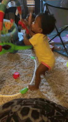 a baby in a yellow shirt is playing on a carpet