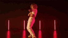a woman is dancing in front of a purple background with neon lights .