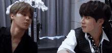 two young men are sitting next to each other and looking at each other .