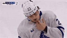 a hockey player is holding his chest while wearing a helmet and a jersey with a maple leaf on it .