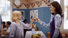 two women are standing next to each other in a room with flowers on the table .