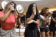 a group of women singing into microphones in front of a sign that has the number 15 on it