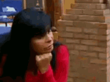 a woman in a red sweater is standing in front of a brick wall .