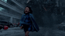 a little girl in a blue plaid dress is running in a smokey area