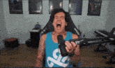 a man is screaming into a microphone while wearing a blue tank top with a white s on it