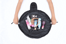a person is holding a black bag filled with makeup and a bottle of perfume