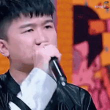 a man is singing into a microphone while wearing a leather jacket .