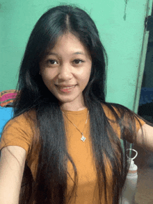 a woman with long black hair wearing a yellow shirt and a necklace