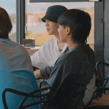 a group of people are sitting in chairs in front of a window . one of the people is wearing a hat .
