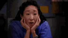 a woman is sitting down with her hands on her face and making a funny face .