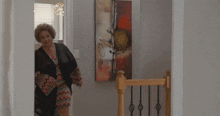 a woman is standing in a hallway next to a staircase and a painting on the wall .