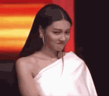 a woman with long black hair is wearing a white one shoulder dress and earrings .