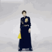 a man in a long black dress is dancing with a yellow fan