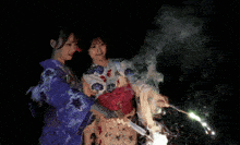 two girls in kimonos are holding sparklers in their hands