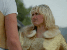 a blonde woman wearing a gold jacket is making a funny face