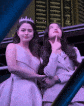 two women standing next to each other with one wearing a crown