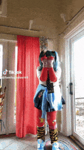 a woman in a costume is standing in front of a red curtain and a window .