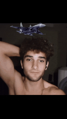 a shirtless man is taking a selfie with a toy plane flying over his head